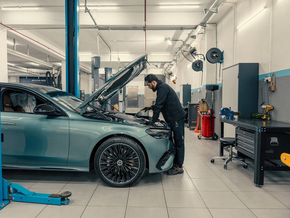 Mécanicien en tenue de travail penché sur le moteur d'une berline, dans un atelier moderne, lumineux et ordonné