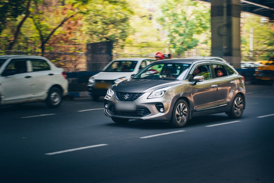 Suzuki Baleno dans la circulation d'une avenue, sous un pont routier